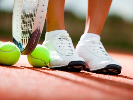 Tennis shoes and two tennis balls on a clay court, symbolizing sports activity and potential foot and ankle injuries in tennis.