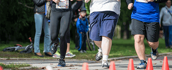 Runners participating in a race, showcasing proper footwear for physical activity, surrounded by spectators and cones marking the course.