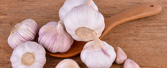 Garlic cloves and bulbs on a wooden spoon, representing a home remedy for athlete's foot.
