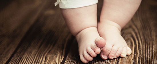 Baby feet standing on wooden floor, symbolizing infant foot development and health in pediatric care.