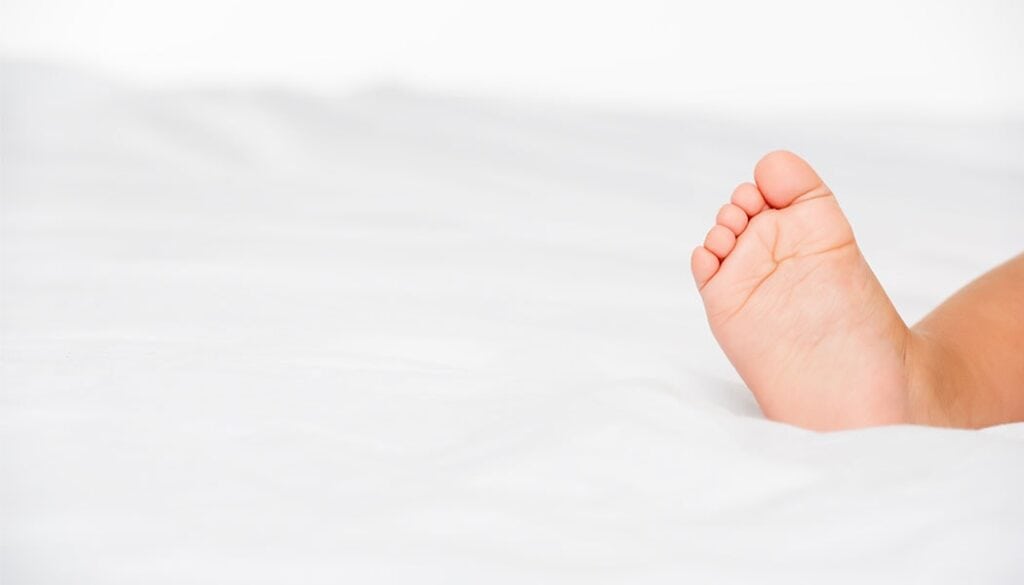 Baby's foot on soft white surface, highlighting potential toe tourniquet syndrome concerns in pediatric foot health.