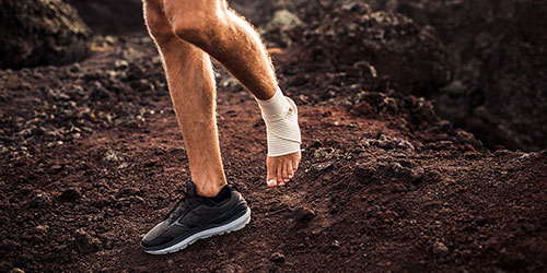 Person with a bandaged ankle running on rocky terrain, illustrating ankle impingement and foot health issues related to injury.