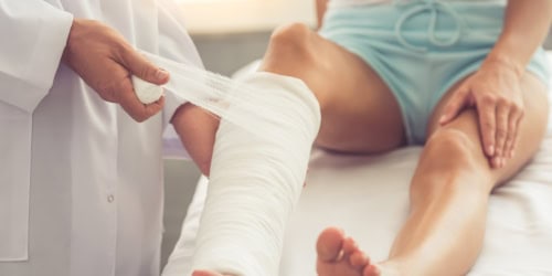Doctor wrapping an injured leg with a bandage, emphasizing urgent foot care and injury treatment.