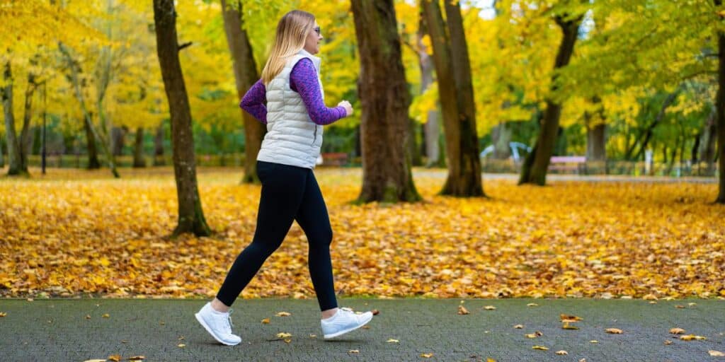 1. Woman walking in autumn park wearing athletic shoes and activewear, showcasing foot health and exercise routines.