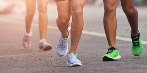 Group of runners in athletic footwear on a paved road, illustrating the importance of proper foot care and gait in maintaining foot health during summer activities.