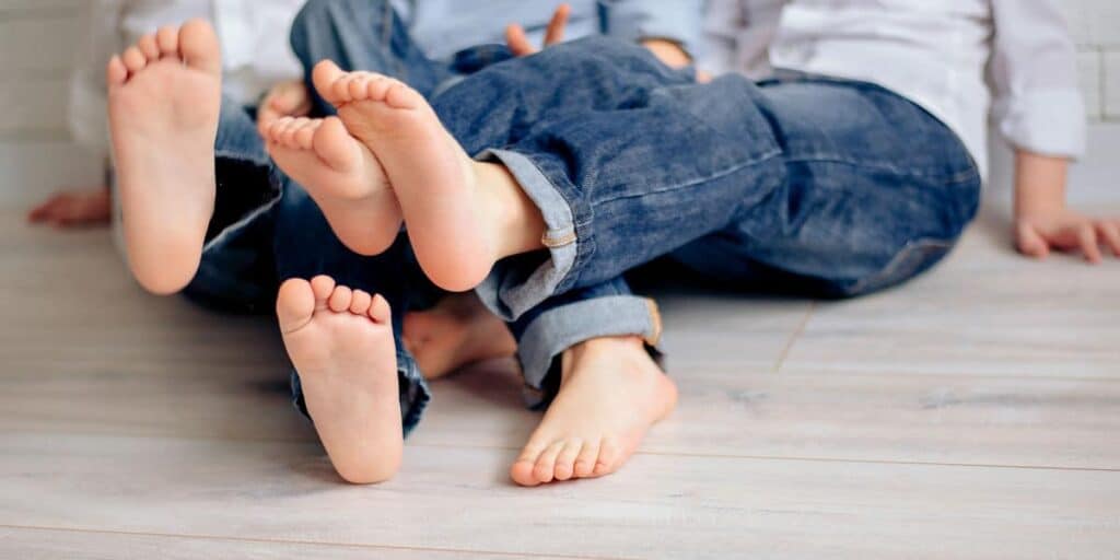 Children's bare feet resting on a wooden floor, illustrating pediatric foot health and conditions like flat feet.