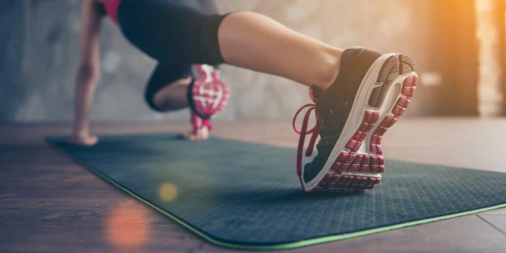 Person performing a workout on a yoga mat, focusing on running form and footwear, emphasizing athletic shoes suitable for runners.