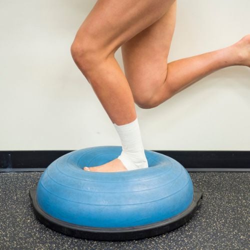 Ankle rehabilitation exercise using a balance trainer with a wrapped ankle for injury recovery and strengthening. Focuses on ankle stability, mobility, and injury prevention, ideal for foot and ankle.