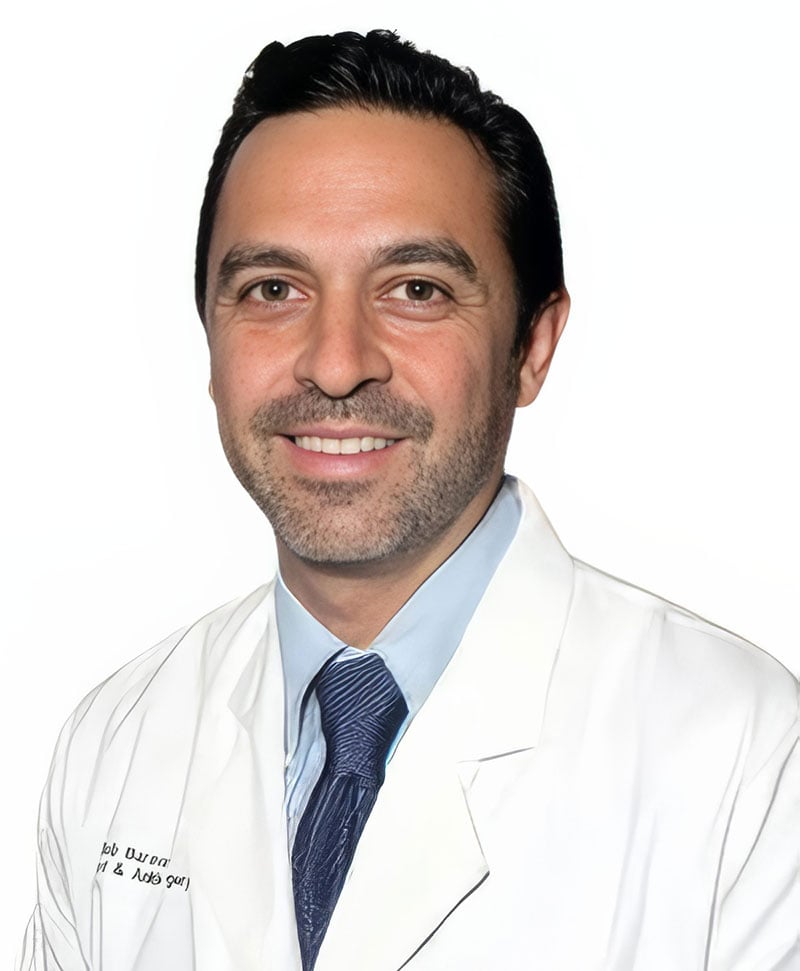Portrait of Dr. Bob Baravarian, a foot and ankle surgeon, smiling in a white coat with a blue tie, against a plain white background.