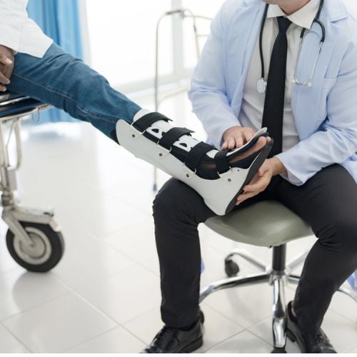 Doctor examining patient's leg with a medical brace in a clinical setting.